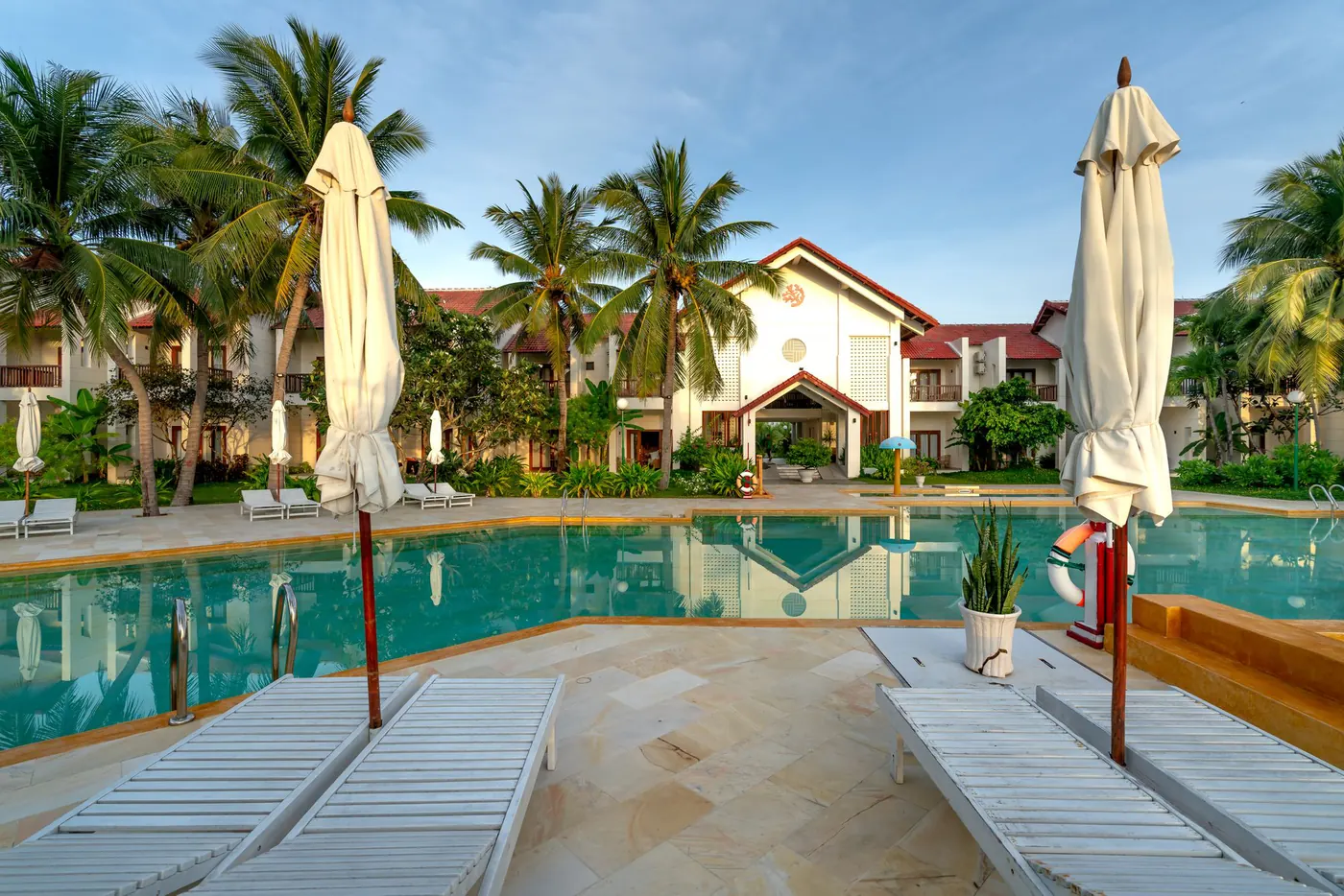 Resort pool ringed by palm trees, parasols and empty loungers