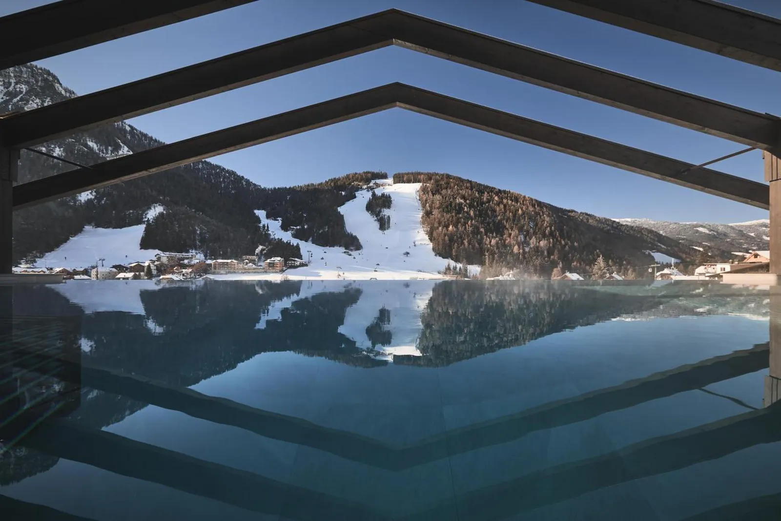 Rooftop infinity pool at AMA Stay with snowy Kronplatz slopes reflected in the water