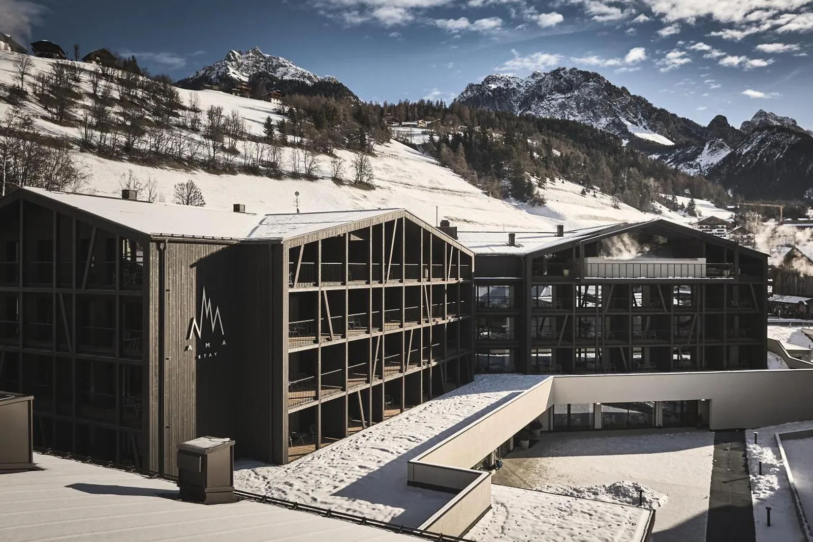 AMA Stay's timber-clad building in snow at the foot of Kronplatz