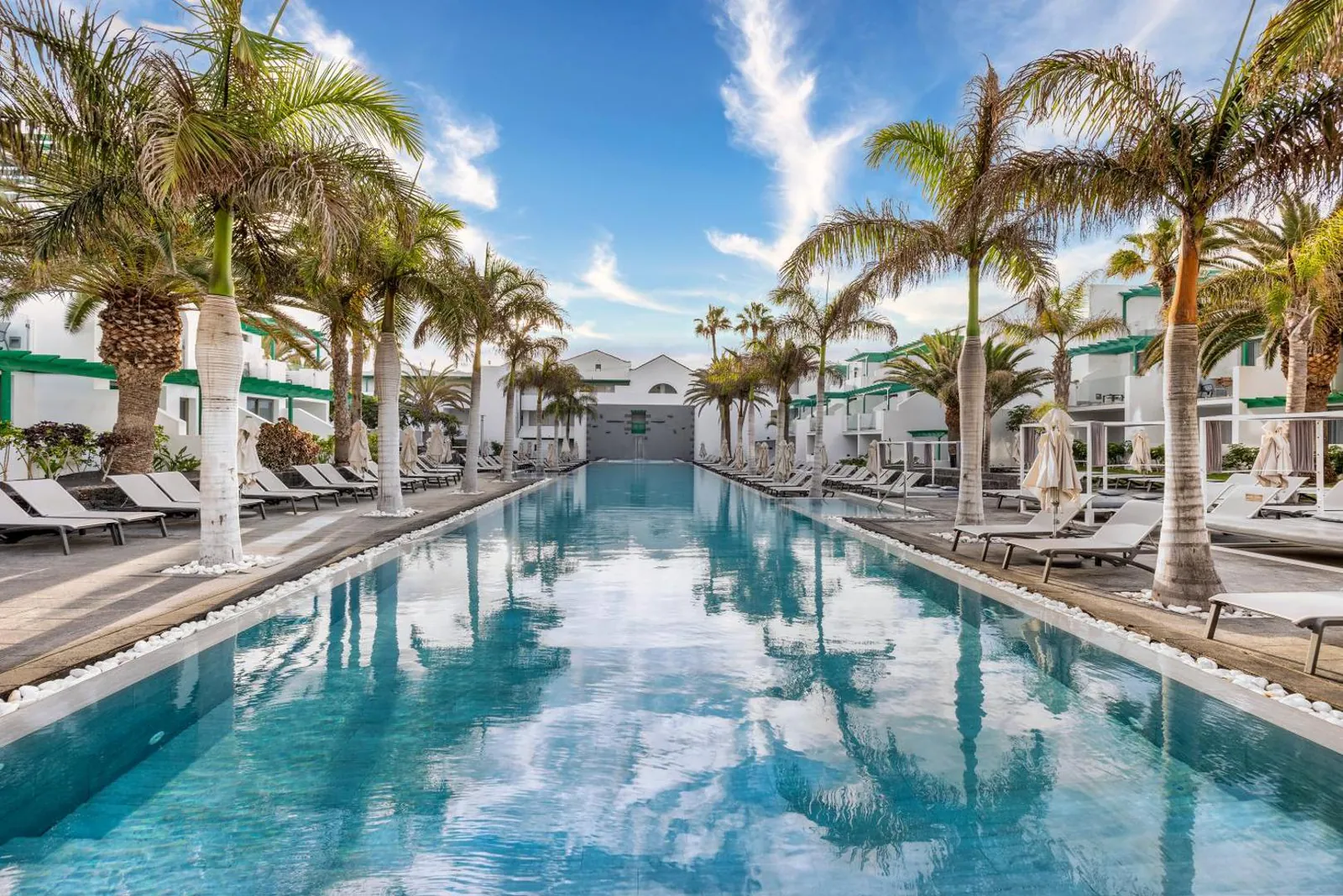 Long outdoor pool lined with palms and white loungers at Barceló Teguise Beach