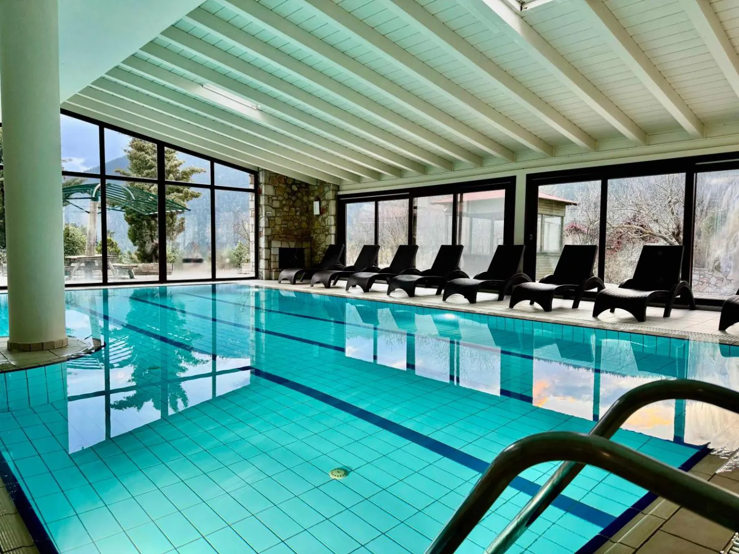 Long indoor pool with loungers lined up beside large windows at Skamnos Arachova