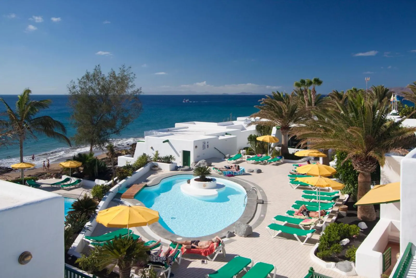 Kidney-shaped pool with yellow umbrellas above the sea at Bungalows Velázquez