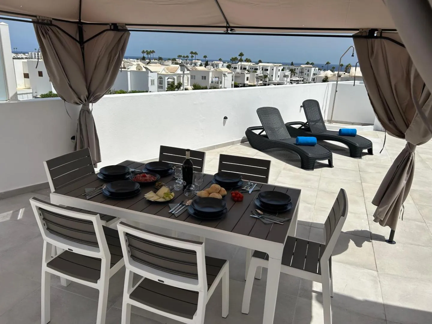 Curtained gazebo with a dining table and loungers on the pool terrace