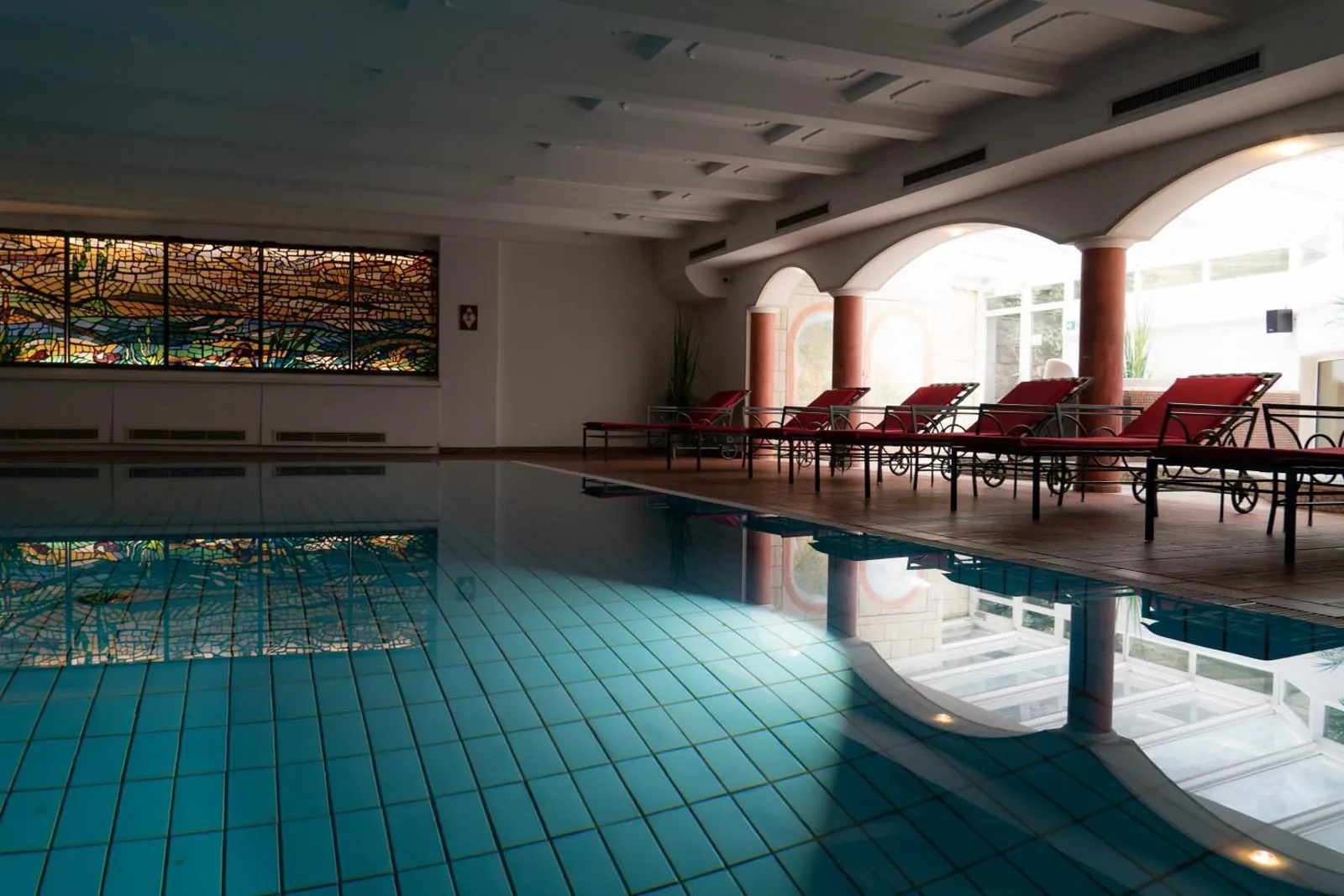 Indoor pool under arched windows with loungers along the side