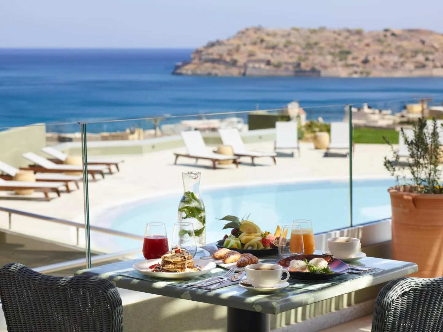 Pool deck with breakfast on the table and Spinalonga across the water