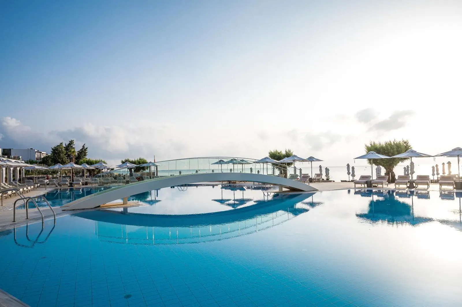 Curving pool with a footbridge and the sea beyond the loungers