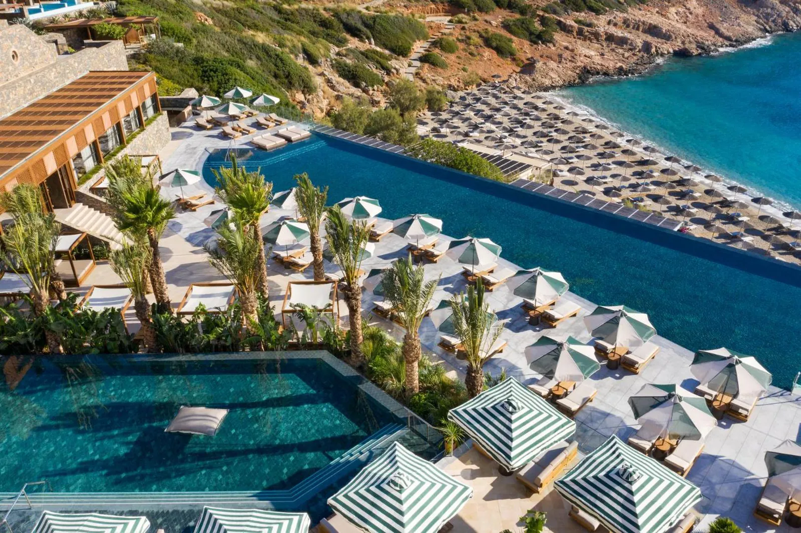 Aerial view of the infinity pool's edge and umbrella-lined terraces above the beach