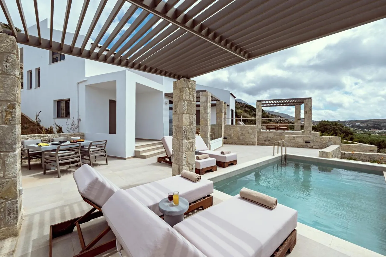 Loungers under a timber pergola next to a villa's private pool