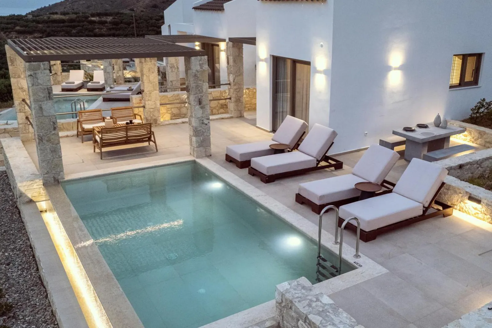 The private pool lit up in the evening, with loungers along the deck