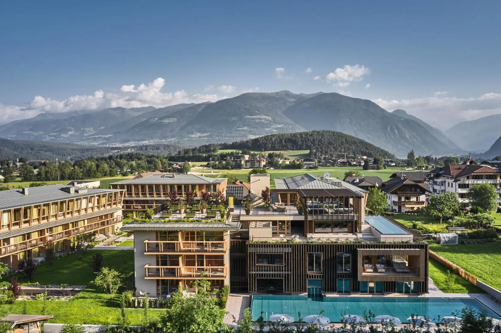Aerial view of the hotel's timber buildings, the rooftop pool and the long sports pool below the mountains