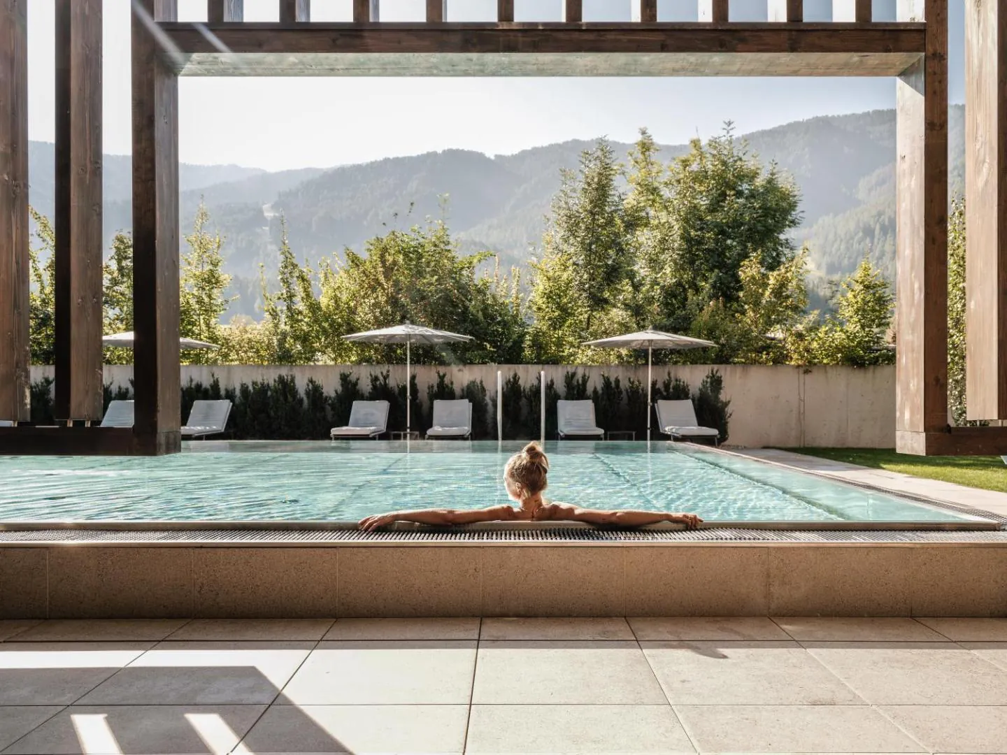 Guest resting at the edge of the outdoor pool, framed by timber beams, with wooded hills behind