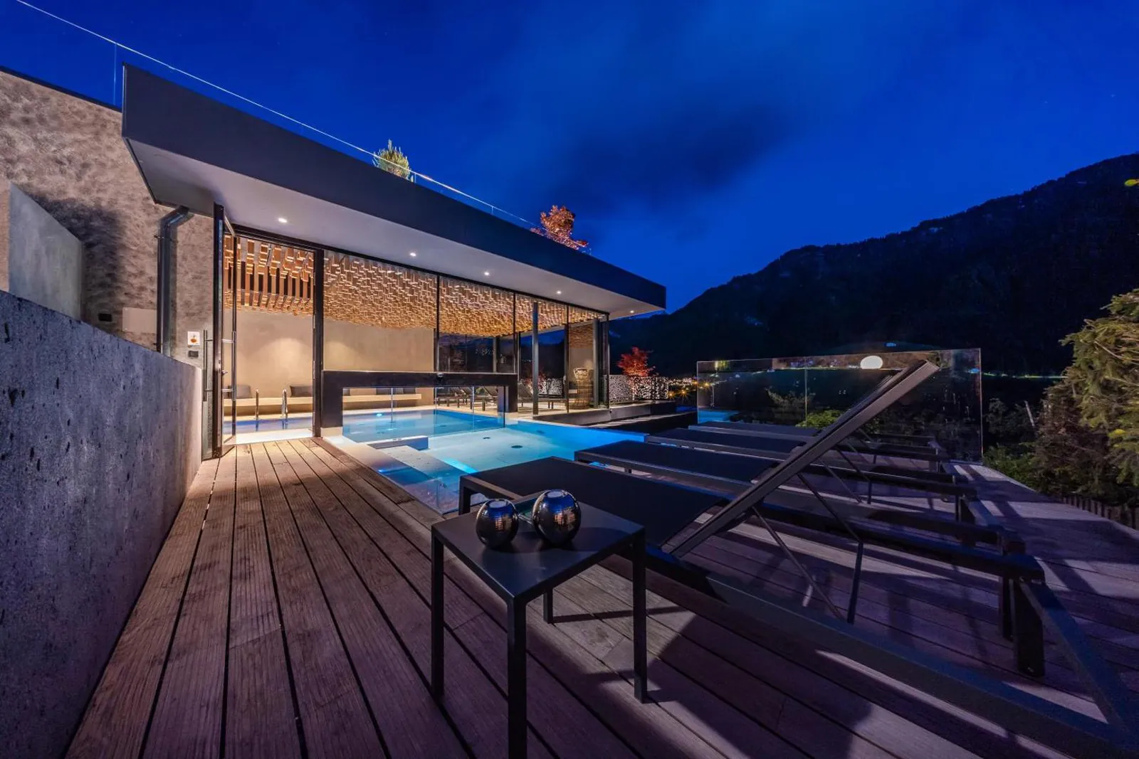 Outdoor section of the Gran Tubla pool on a wooden deck with a glass edge, Val Gardena mountains at dusk
