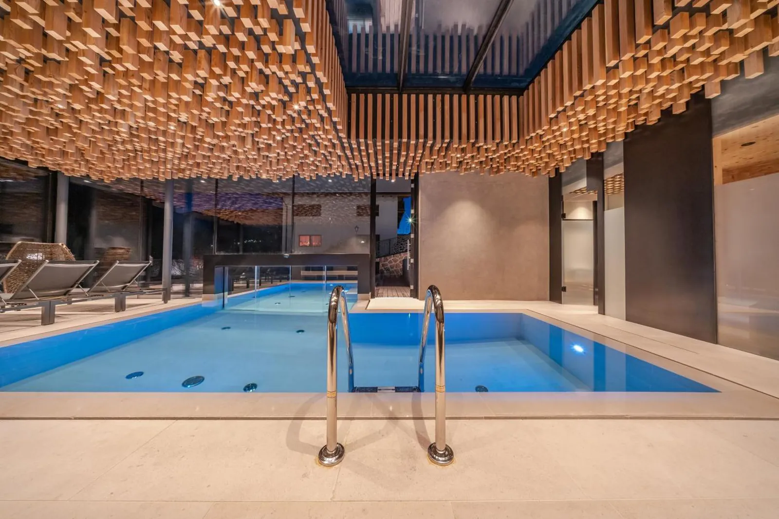 Indoor part of the pool with loungers along the glass wall and the steps into the water