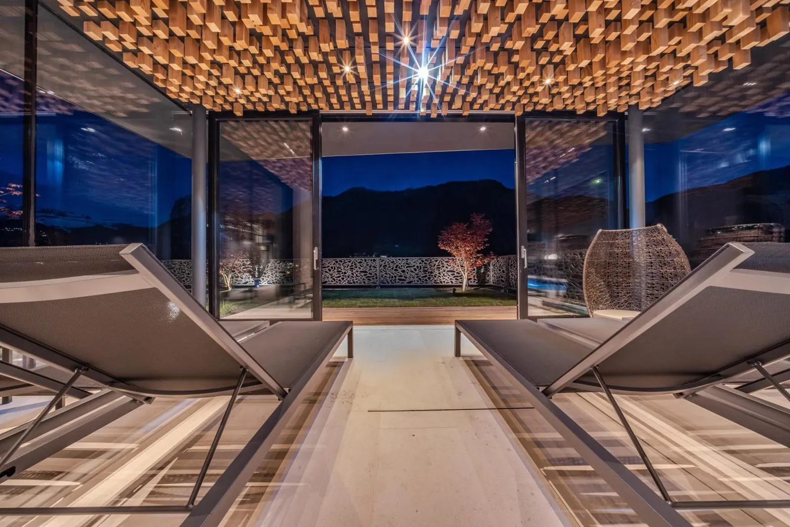 Loungers in the relax area facing glass doors onto the garden and the mountains at night
