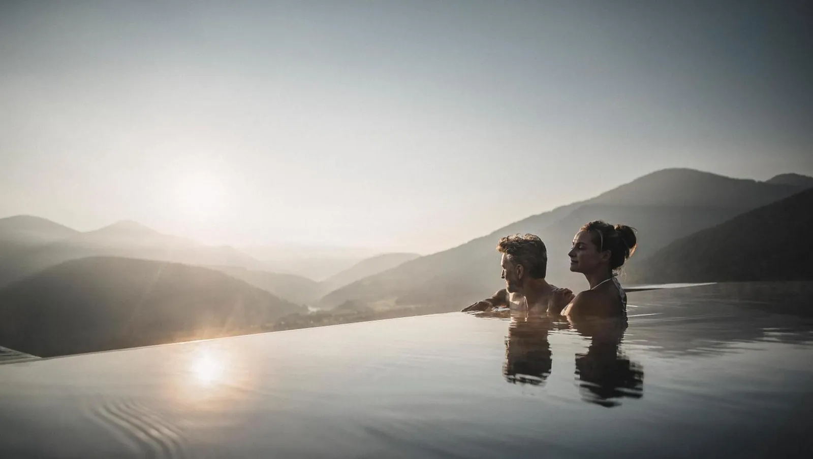 Two guests at the infinity edge of the Sky Pool at sunset, looking over the Pusteria valley