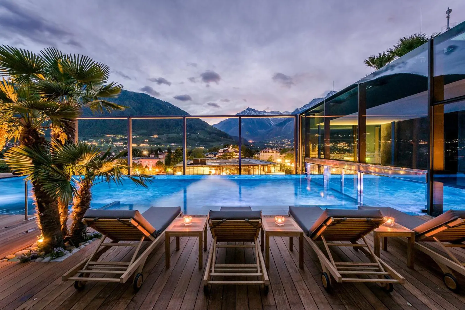 Rooftop pool and loungers lit up at night above the lights of Merano