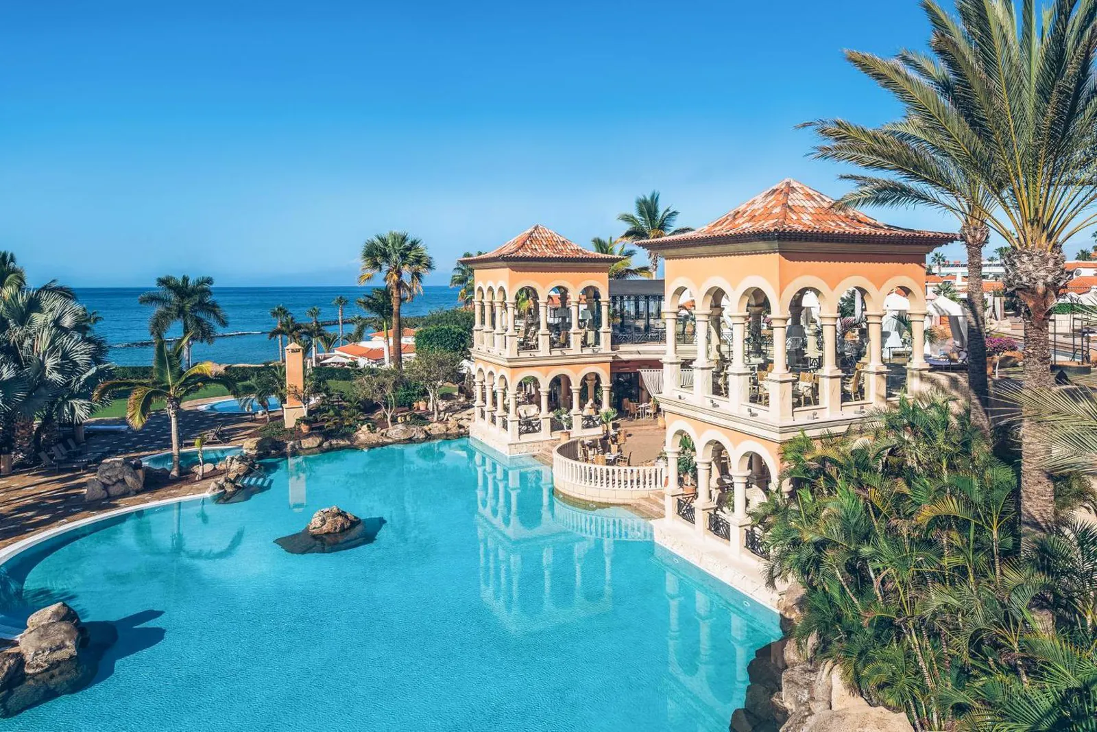 Heated outdoor pool wrapping around the arcaded main building at JOIA El Mirador, with the Atlantic beyond