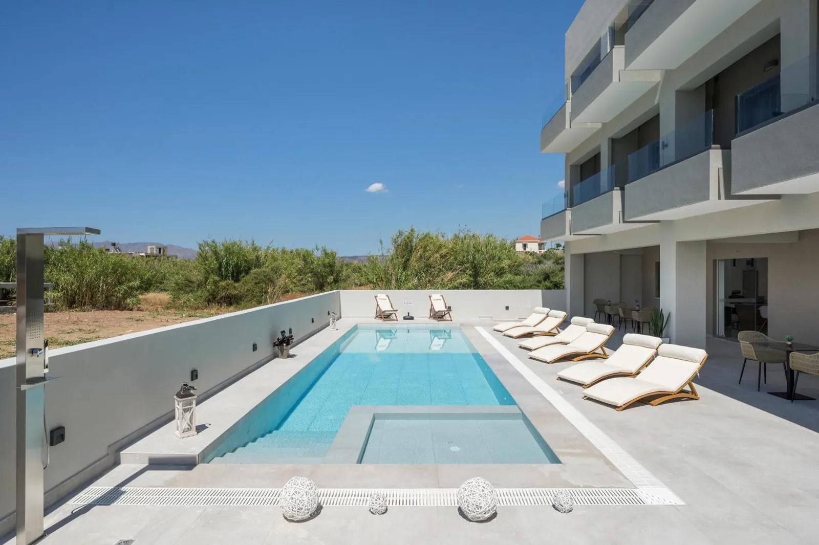 Long outdoor pool with a shallow ledge and white loungers beside Kallistefan