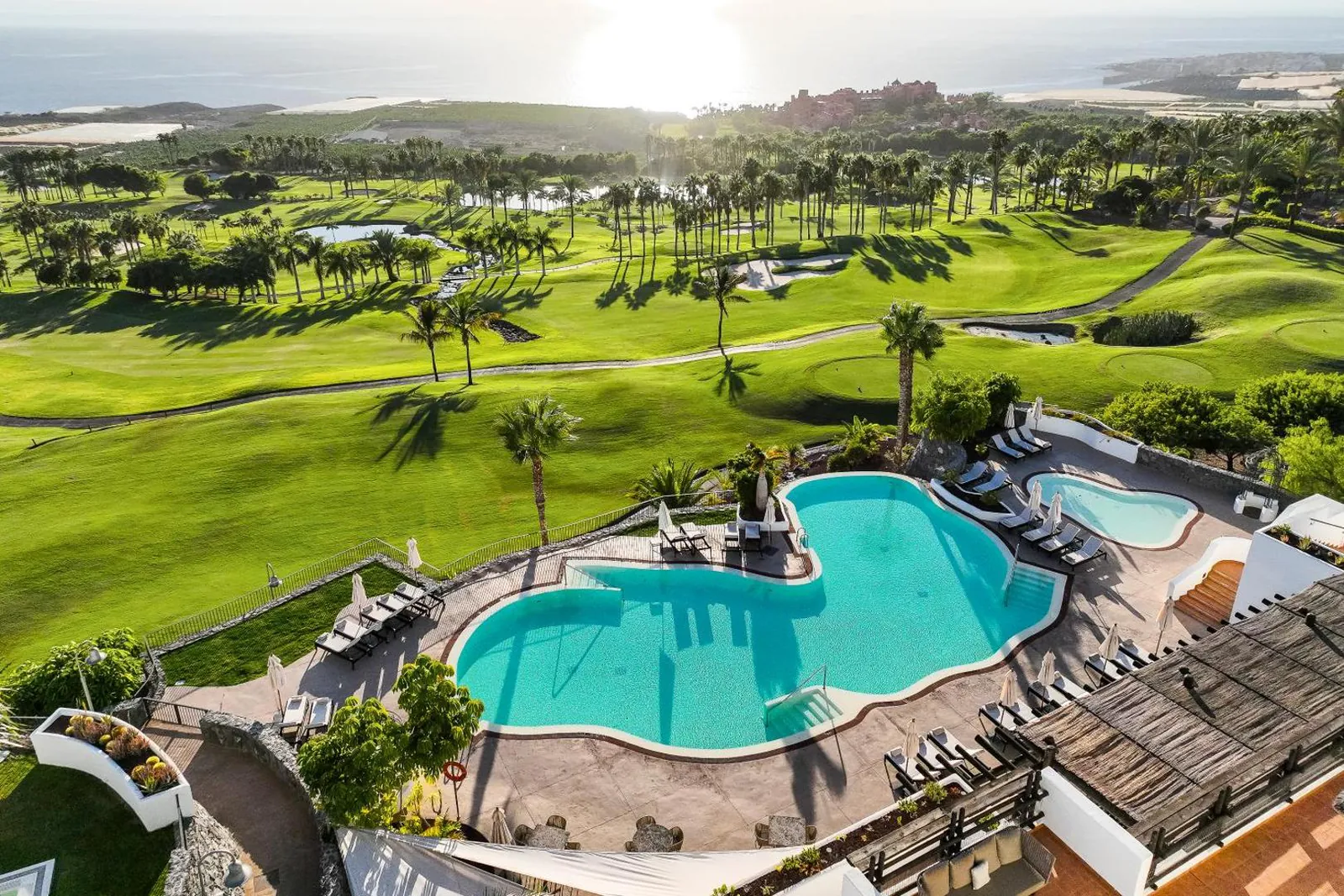 Curving pool and loungers below the white suites, with the golf course beyond