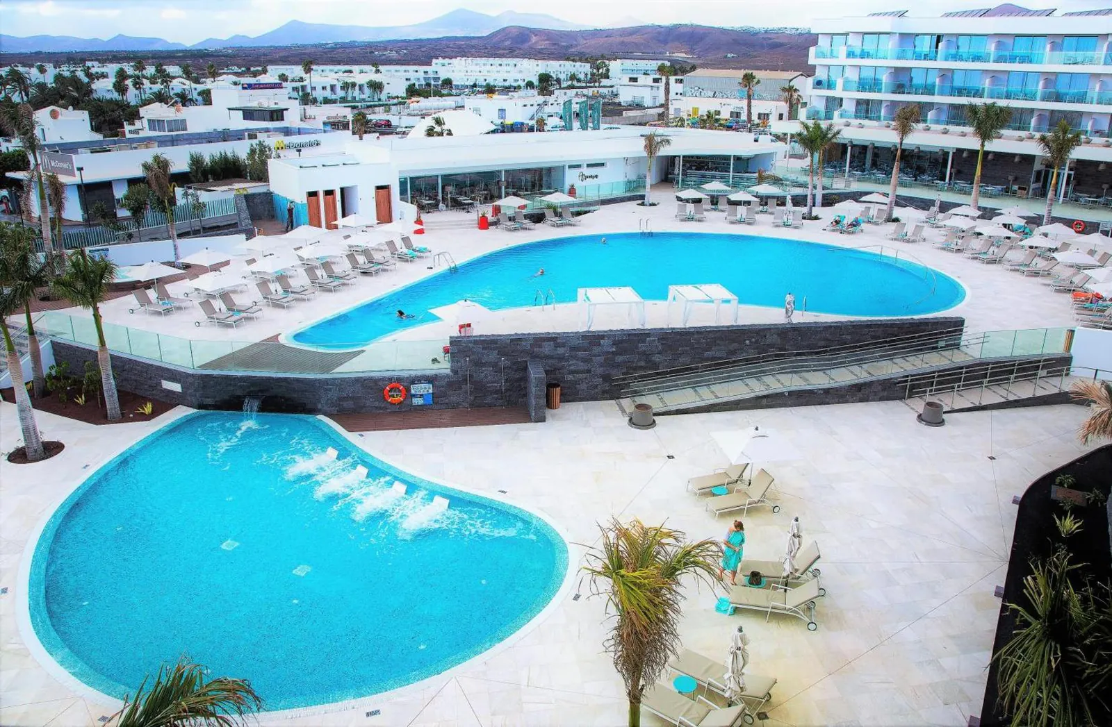 Two curving pools side by side, the larger one edged with loungers