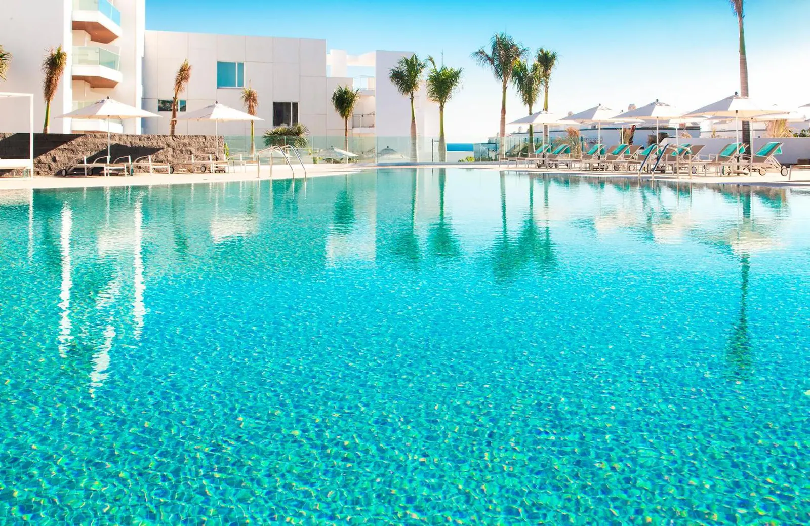 Clear turquoise pool water with palms and loungers along the far edge