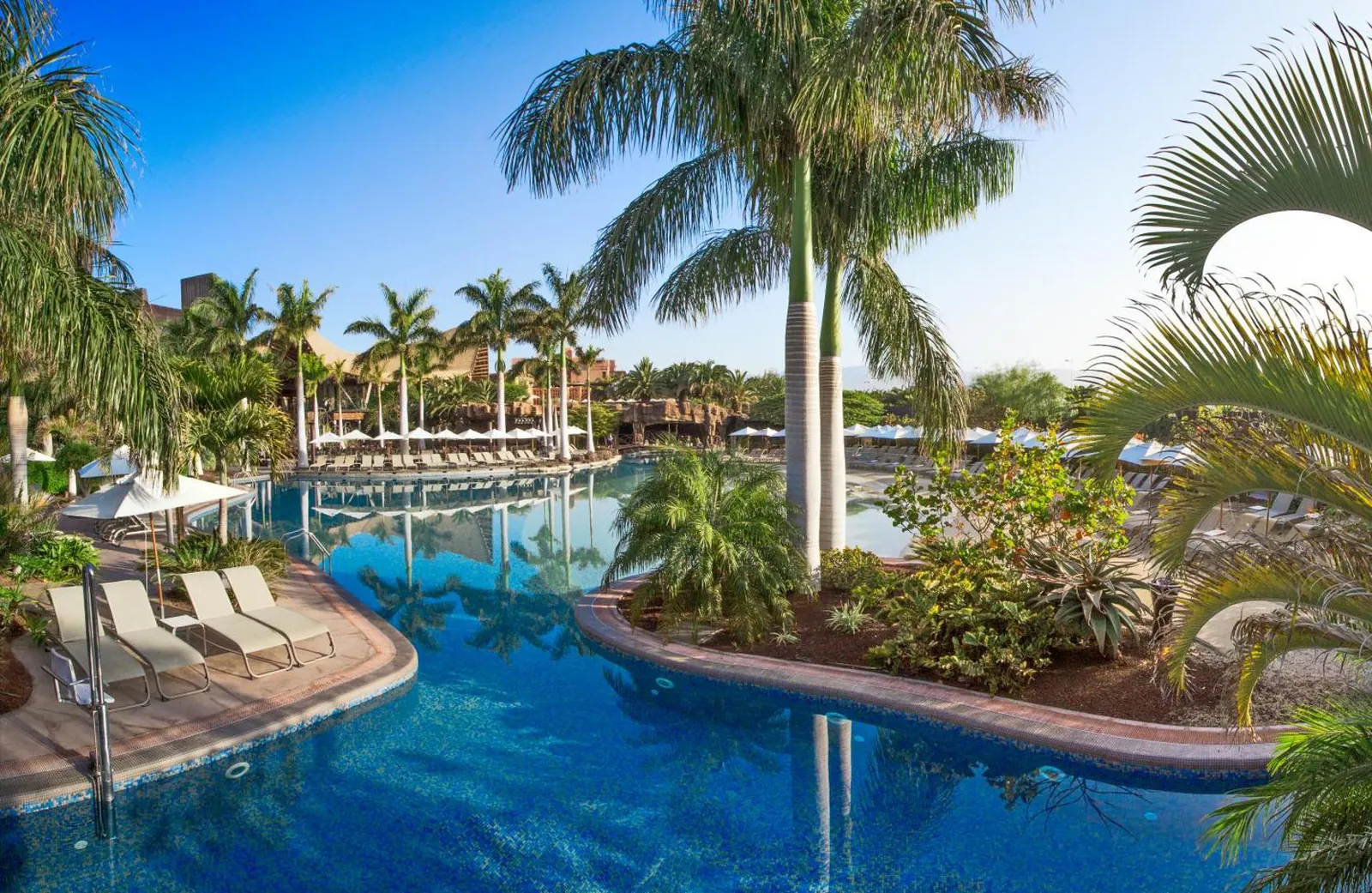 River-shaped pool winding between palm trees and loungers at Lopesan Baobab Resort