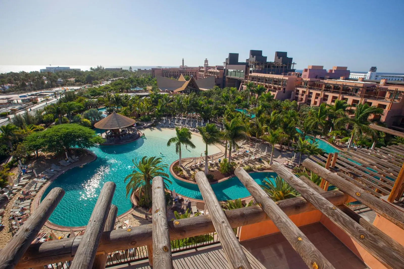 Aerial view of the pools curving through the tropical garden, with Meloneras and the sea beyond