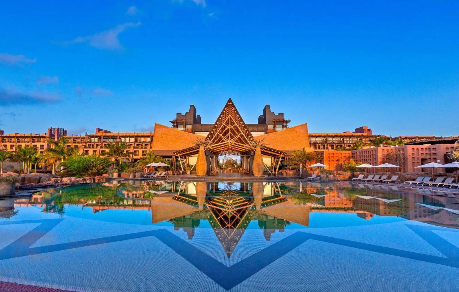 Still pool reflecting the resort's thatched African-style main building at dusk