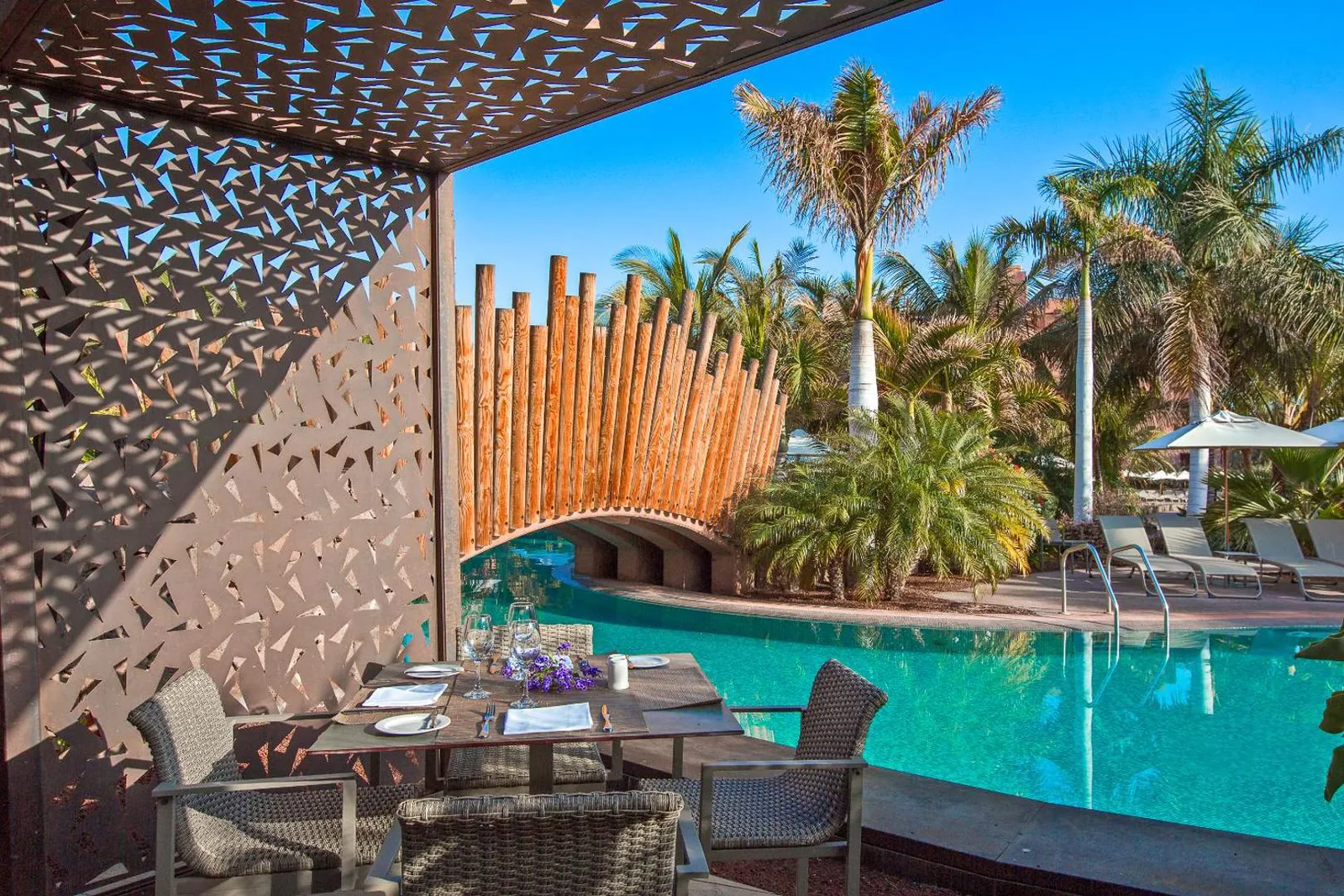 Poolside terrace under a carved wooden canopy beside the water