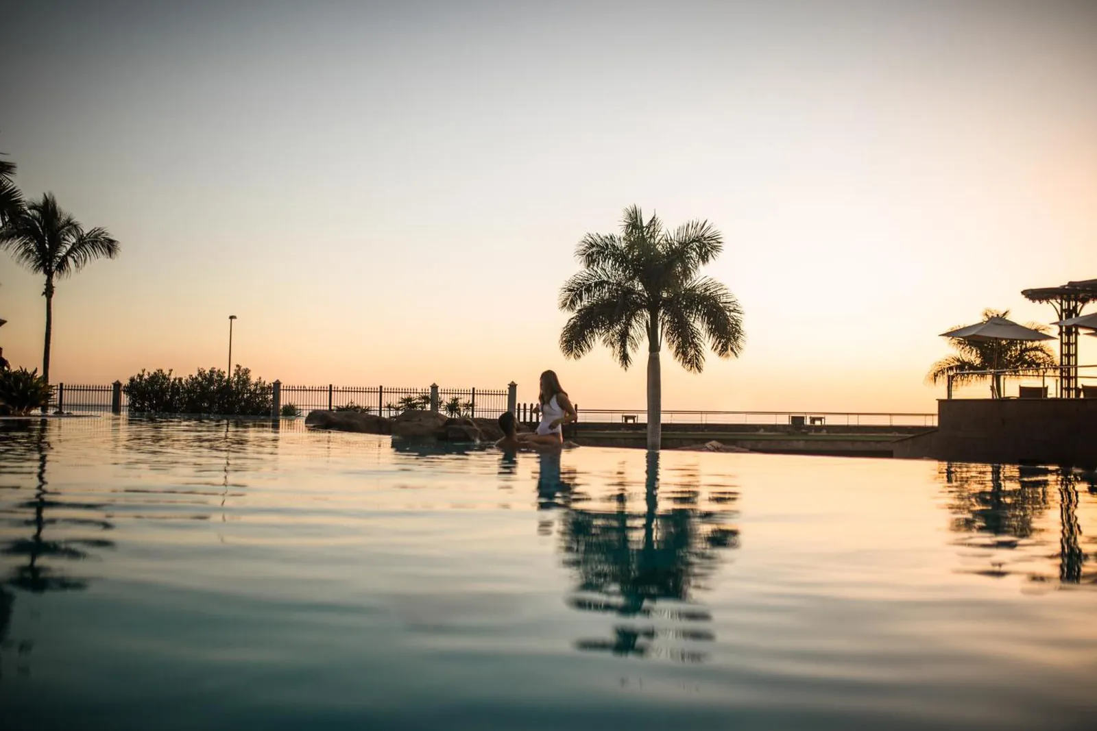 Infinity pool at sunset with palms and the ocean beyond