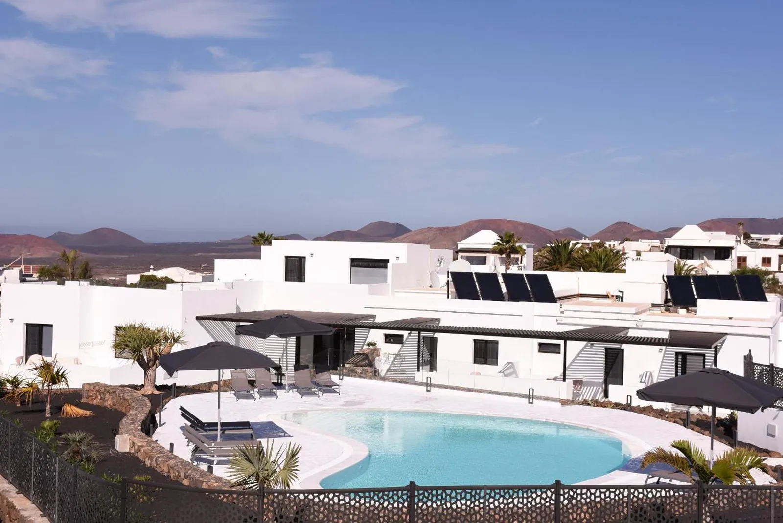 View over the retreat's white buildings, pool and parasols towards the volcanic landscape