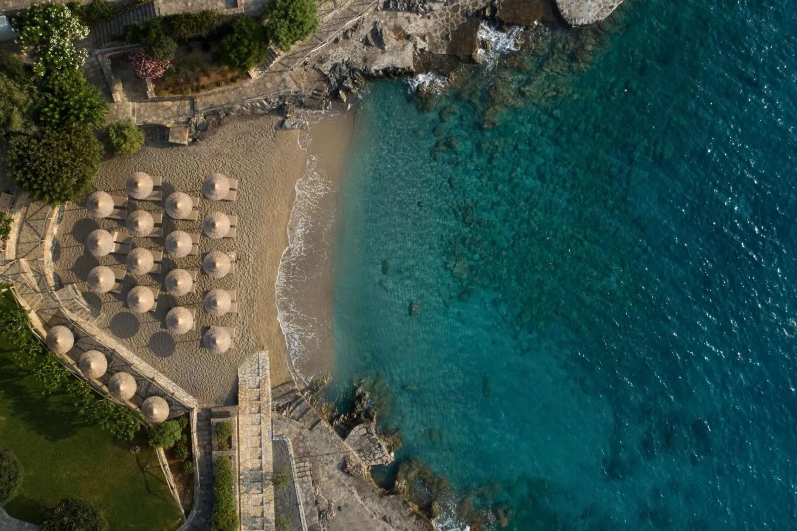 The resort's sandy cove from above, with sunbeds lined up by clear water