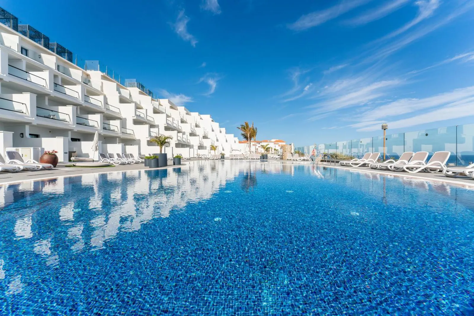 Long outdoor pool in front of the white terraced room blocks, with sun loungers along the glass edge