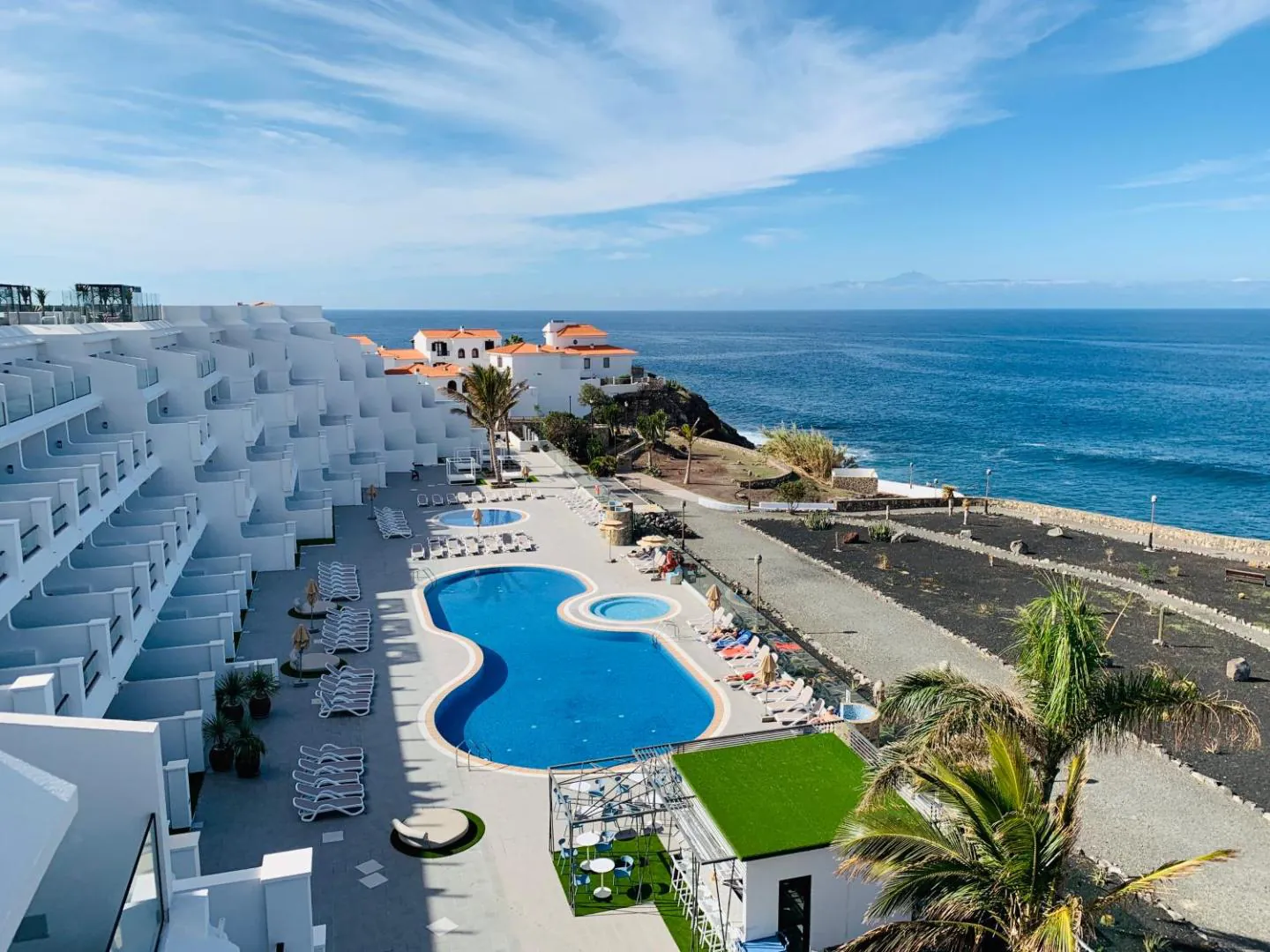 Aerial view of the curved pool and lawn below the hotel terraces, with the Atlantic beyond