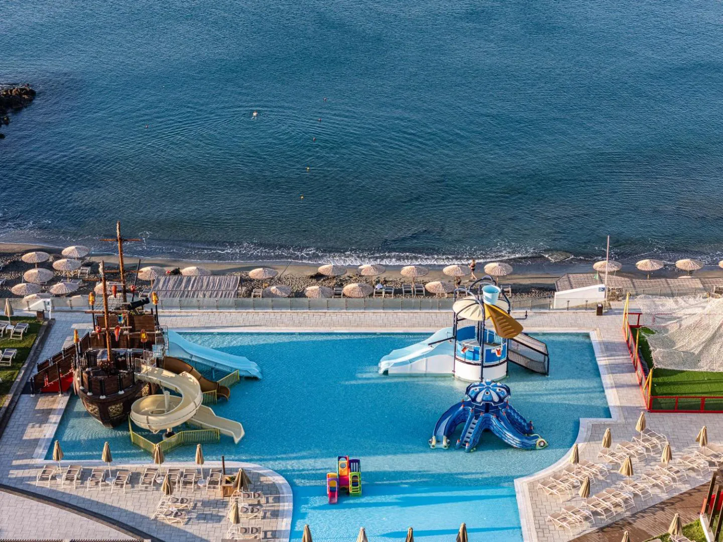 Kids' pool built around a pirate ship with water slides, beside the beach