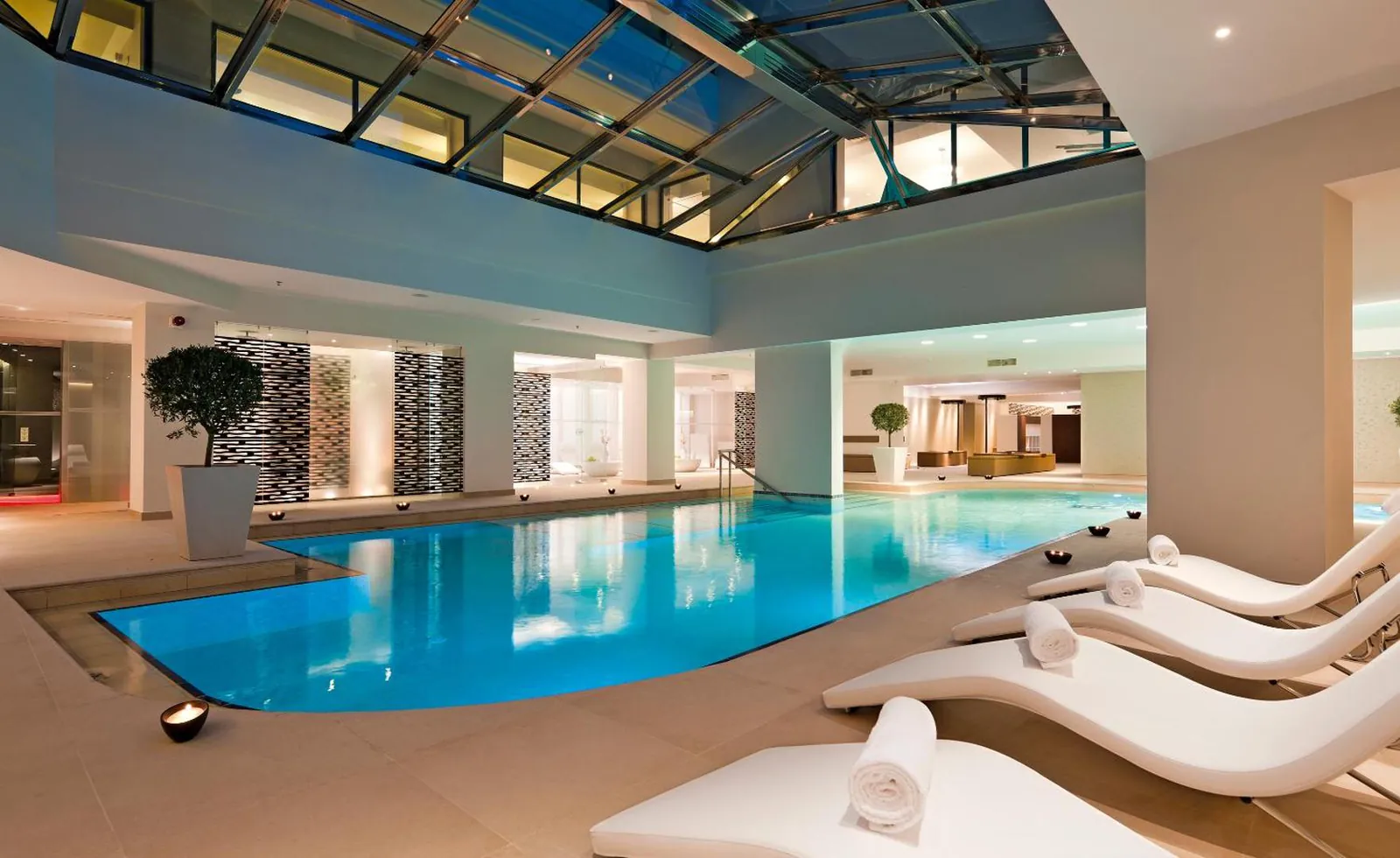Heated indoor pool under a glass roof in the spa, lined with white loungers