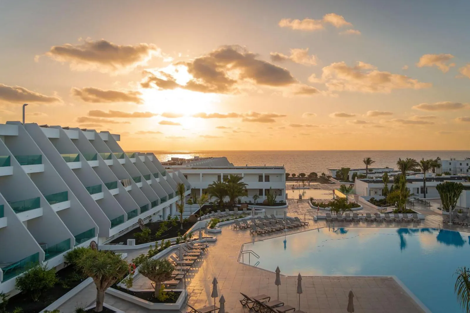 Main pool at sunset below the terraced white wings of the resort, sea on the horizon