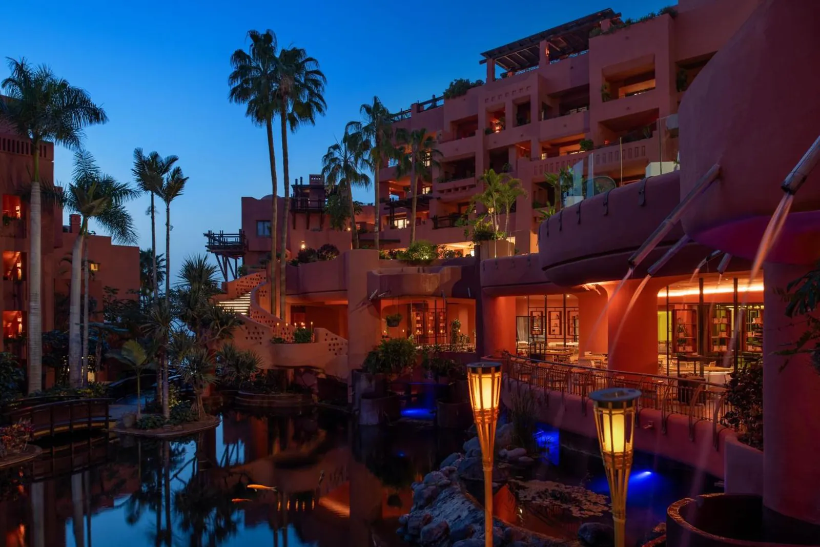 Restaurant terrace beside lit pools of water under palms at night
