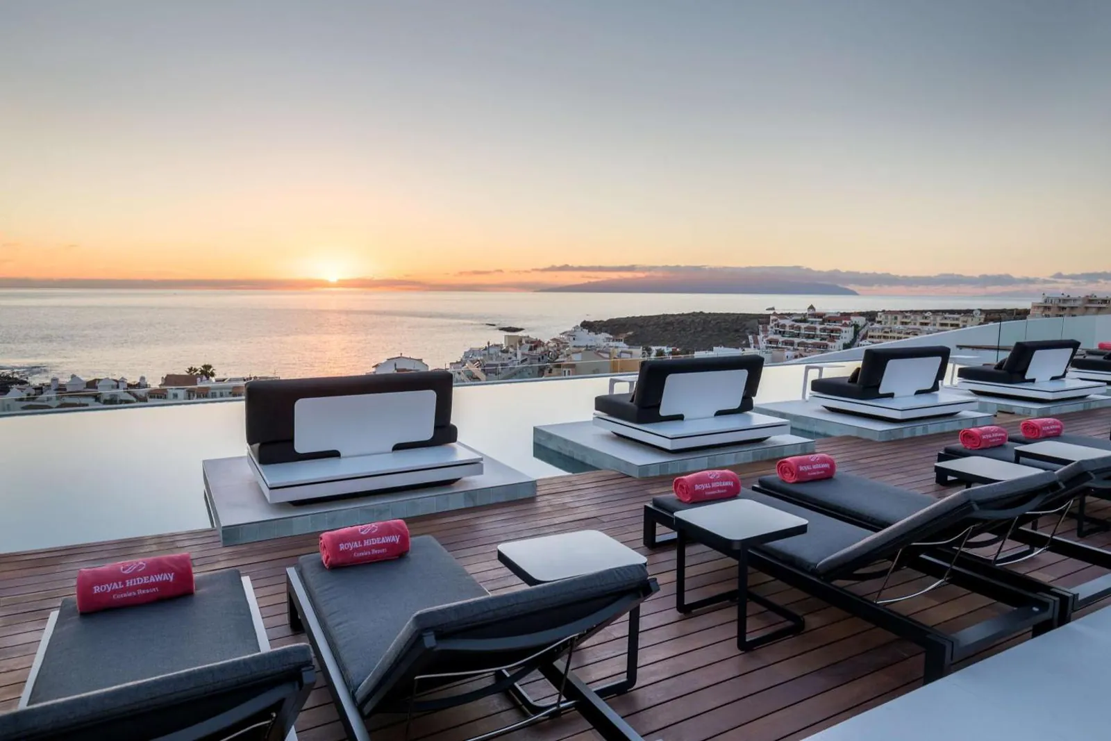 Rooftop infinity pool with loungers at sunset above the coast