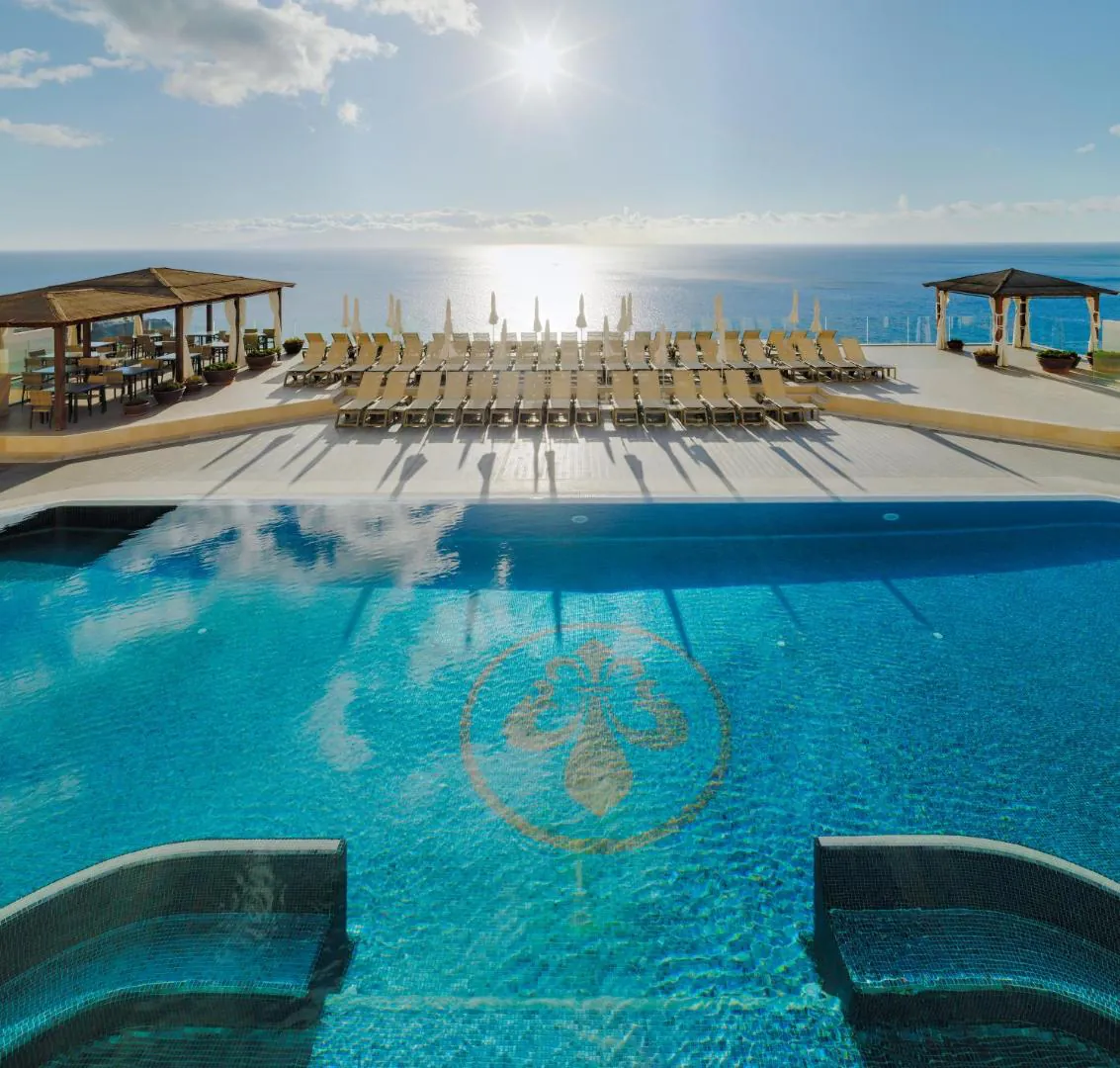 Outdoor pool with the resort crest on its floor and sun loungers at Royal Sun Resort
