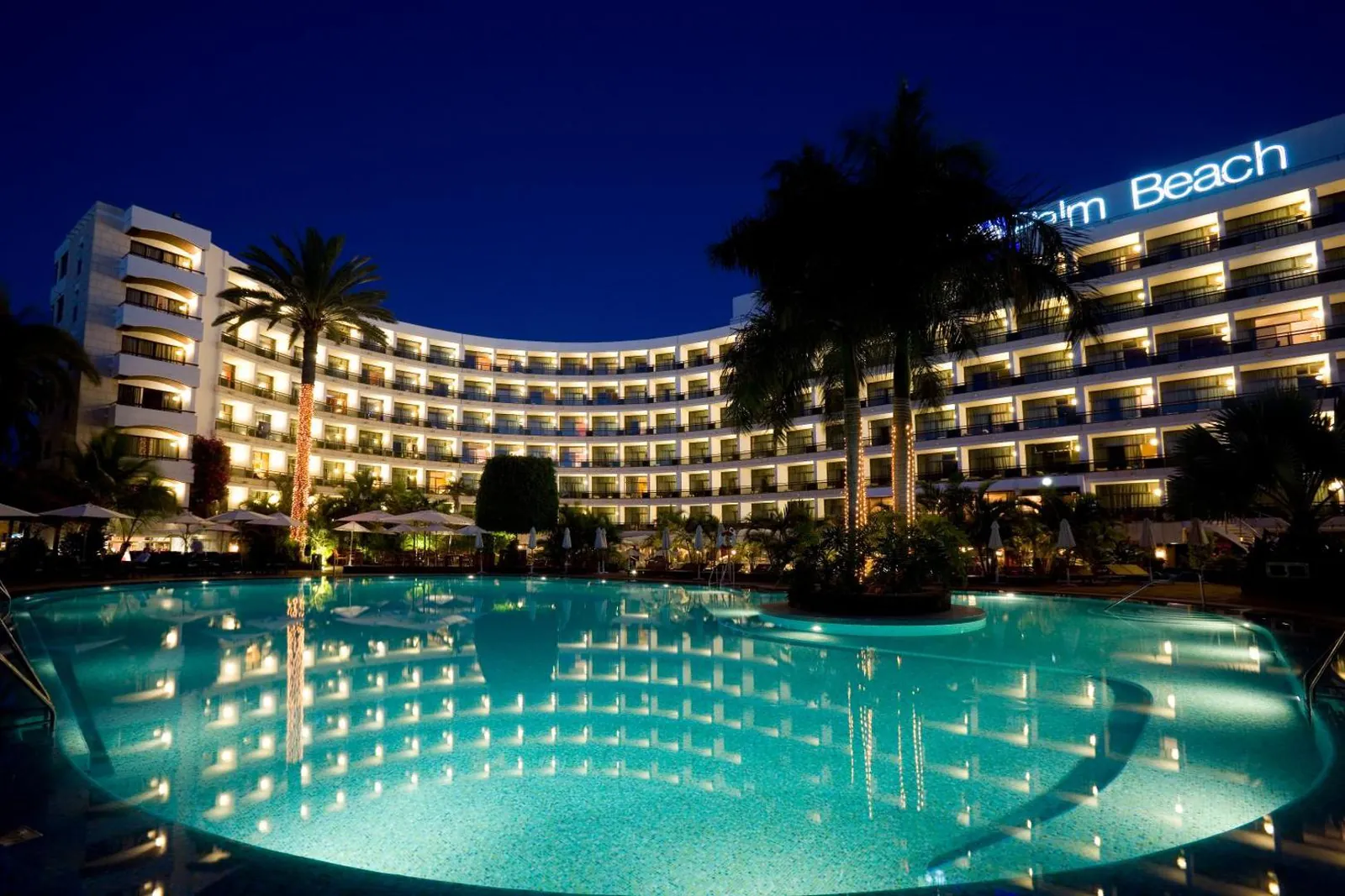 The curved hotel building lit up at night behind the main pool