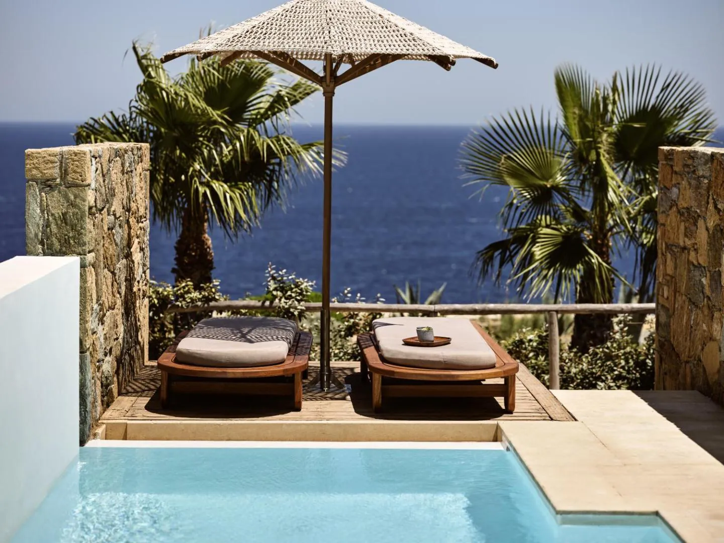 Small pool on a room terrace with two loungers and a parasol facing the sea