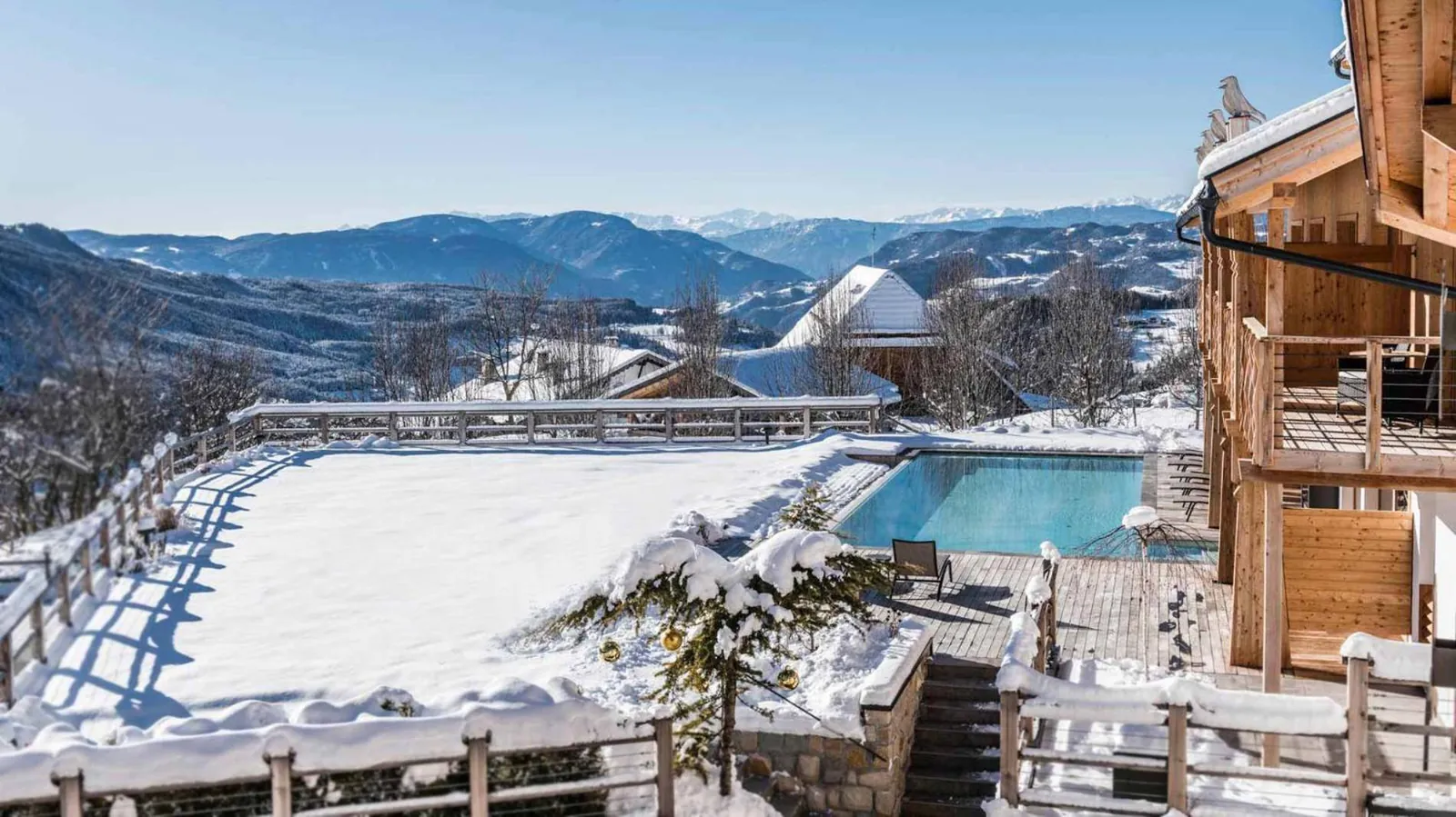 The heated outdoor pool at Sonus Alpis surrounded by snow, with the hotel behind