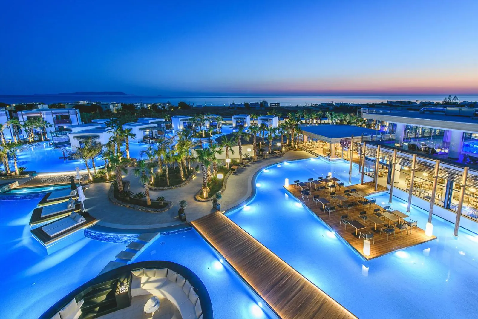 The lit lagoon pool winding through the resort at dusk, sea on the horizon