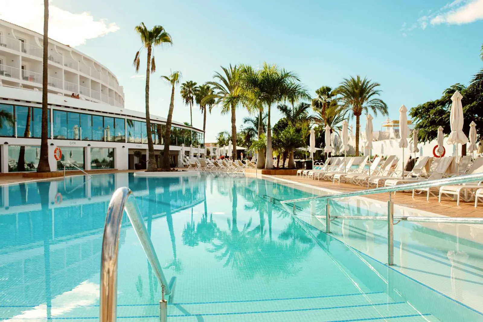 Pool with steps and palms alongside the curved hotel building