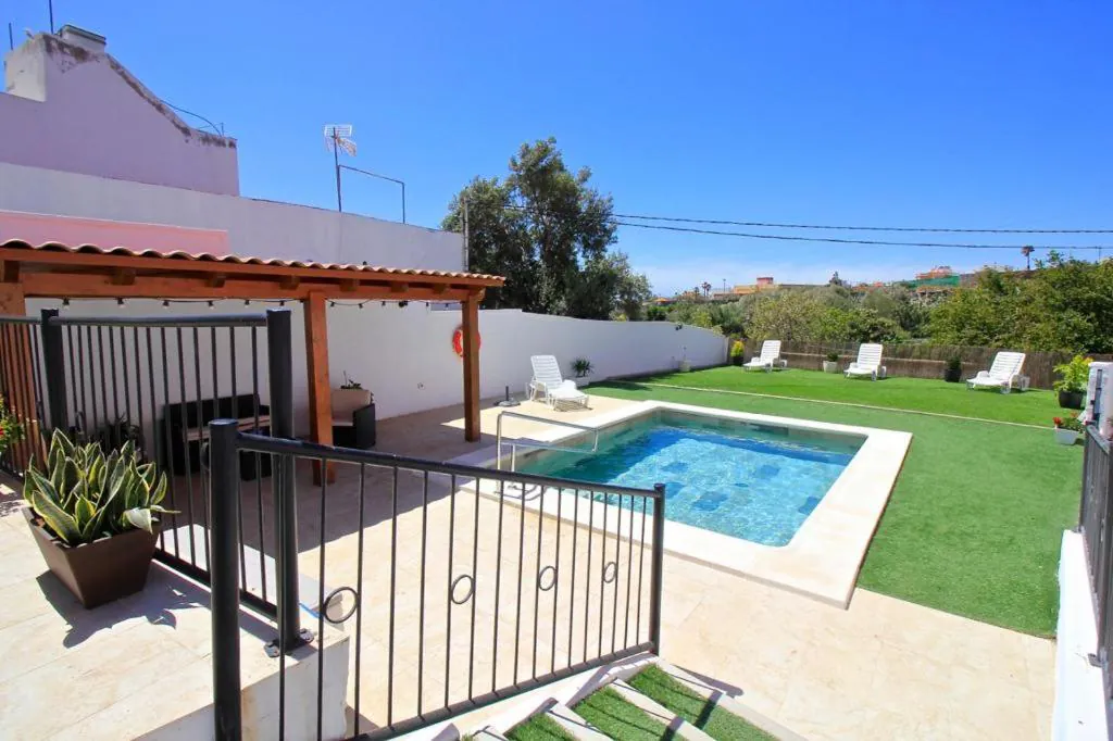 The pool and lawn under a blue sky, with green hills beyond the fence