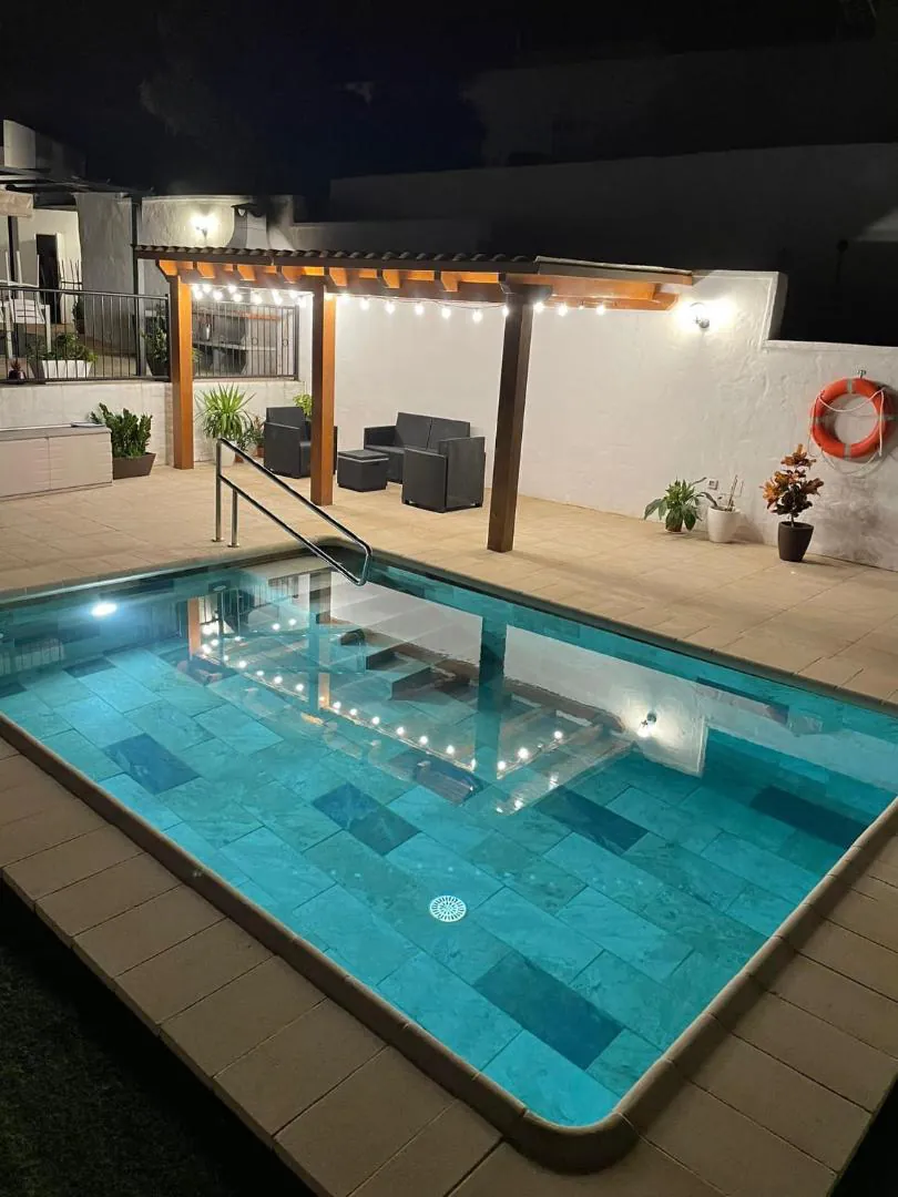 The pool lit turquoise after dark beside the covered terrace