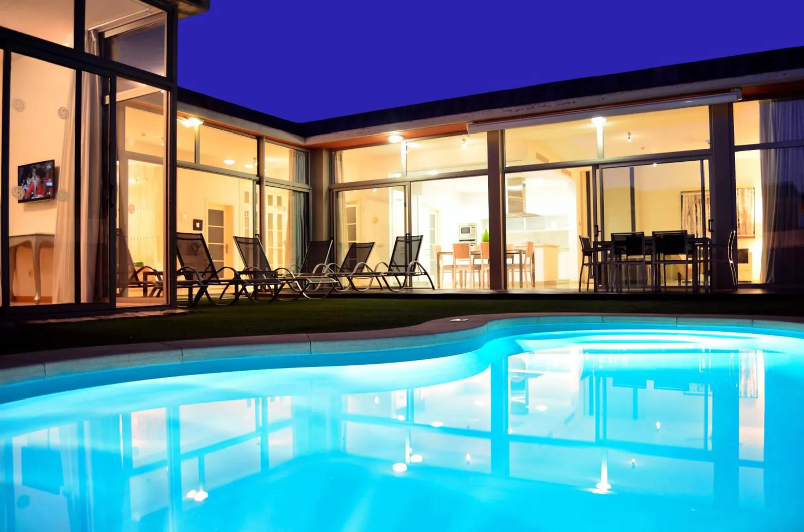 Lit private pool and glass-fronted villa at dusk