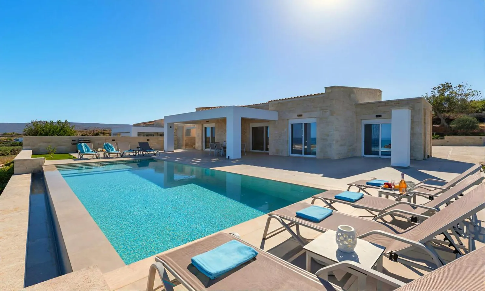 Private pool running along the stone villa, with loungers on the deck and the sea in view