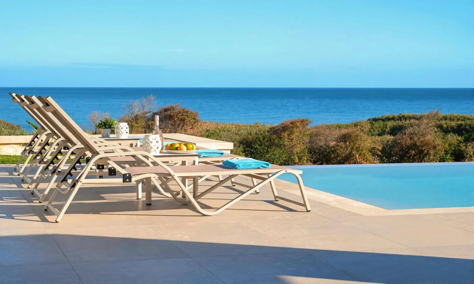 Loungers at the pool's edge looking out over green slopes to the sea